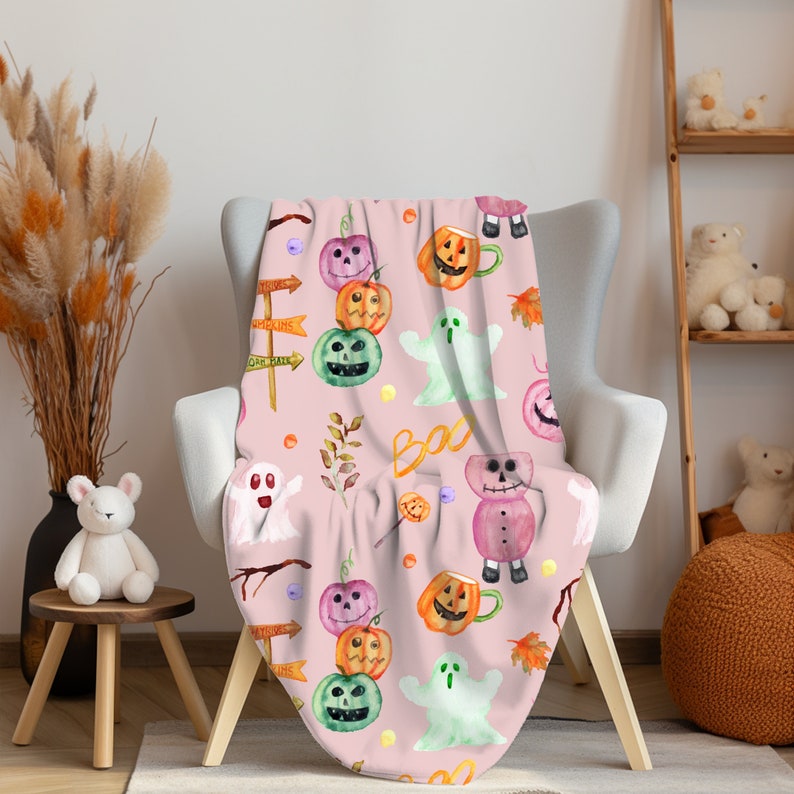 Pu&ograve; includere: Una coperta rosa con tema di Halloween con zucche, fantasmi e un pupazzo di neve. La coperta ha un motivo ripetitivo di questi elementi su uno sfondo rosa.