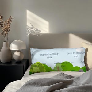 May include: A rectangular pillow with a light blue background featuring a green tree and bush design. The pillow has the text "OVERLAY MOCKUP PNG" printed on it. The pillow is on a bed with a neutral-coloured headboard.