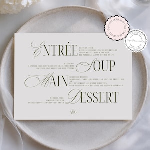 May include: A rectangular wedding menu card with dark green serif typography on a light gray background. The text lists Entrée, Soup, Main, and Dessert courses with descriptions, including Gazpacho, Mushroom Risotto, and Beef Tenderloin, plus A&G initials.
