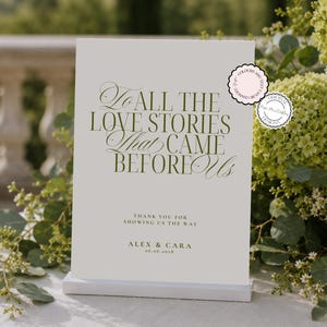 May include: A rectangular white sign with dark green text reading: To ALL THE LOVE STORIES That CAME BEFORE Us, THANK YOU FOR SHOWING US THE WAY, ALEX & CARA, 06.06.2028. Two circular badges are present, one stating COLOURS AND TEXT CAN BE CHANGED.