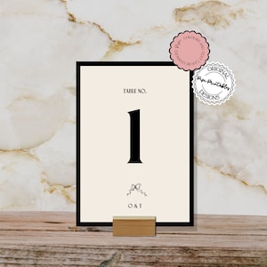 May include: Black and white table number card with the number "1" in a bold font. The card is on a wooden stand and has the text "TABLE NO." and "O & T" printed on it.