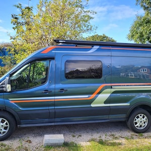 Könnte beinhalten: Ein blau-grüner Campervan mit orangefarbenen und weißen Streifen. Das Fahrzeug hat eine schwarze Markise und getönte Scheiben. Es steht auf Gras mit einem Steinblock davor. Der Himmel ist blau mit Wolken.