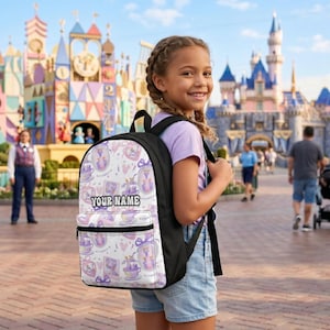 May include: A black and white backpack with a white front panel featuring a repeating pattern of teacups, hearts, and bows in shades of purple. The text "YOUR NAME" is printed on the front. The backpack has a black back and straps.