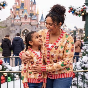 Puede incluir: Una rebeca beige con botones que presenta un patrón repetitivo de cabezas de Mickey y Minnie Mouse estilo pan de jengibre, ribetes a rayas rojas y blancas y un fondo a cuadros. La prenda de punto tiene mangas largas y cuello en V.