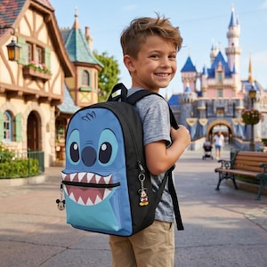 May include: A blue and black backpack featuring a cartoon character face with large eyes and a wide grin. The backpack has a front pocket and a Mickey Mouse keychain. The background shows a theme park with a castle.