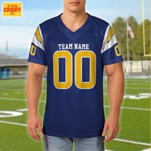 May include: Navy blue football jersey with yellow detailing and the number "00". The jersey features a V-neck and white and yellow lightning bolt design on the shoulders. The text "TEAM NAME" is above the numbers.