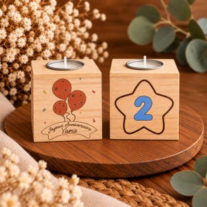 May include: Two light-colored wooden cube candle holders with metal inserts. One cube features a red balloon graphic and the text Joyeux Anniversaire Yanis. The other cube displays a blue number 2 inside a brown star outline.