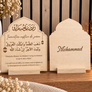 May include: Two light-colored wooden plaques with arched tops, each resting on a rectangular wooden base. The left plaque features Arabic calligraphy, the text "Invocation rupture du je&ucirc;ne," and a prayer in Arabic and French. The right plaque displays the name "Mohammad" in a dark script font.
