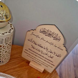 May include: A light-colored wooden plaque with an arched top, featuring engraved Arabic calligraphy and French text. The inscription includes the phrase Invocation Pour faciliter les choses, followed by Arabic script and phonetic transliteration.