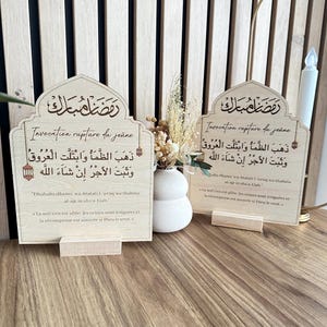 May include: Two arched light-colored wooden plaques featuring Arabic calligraphy and French text titled Invocation rupture du je&ucirc;ne. The plaques include the phrase Dhahaba dhama wa-btalati l-uruq wa thabata al-ajr in sha-a-Llah and its French translation.