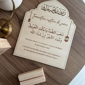 May include: A light-colored wooden plaque with an arched top featuring Arabic calligraphy, the text "Invocation rupture du jeune," and the transliterated and translated prayer for breaking the fast. Two small lantern icons flank the central text.