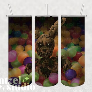 Op de afbeelding: Een groene en bruine animatronische konijn met gloeiende ogen staat in een ballenbak gevuld met kleurrijke ballen. De achtergrond is zwart.