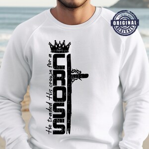 Peut inclure: Un t-shirt blanc à manches longues avec un motif graphique noir représentant une couronne et une croix. Le texte "He traded His crown for a CROSS" est imprimé verticalement sur le t-shirt.