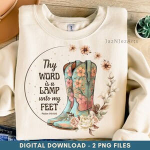 May include: A cream-coloured sweatshirt with a watercolour design of turquoise cowboy boots decorated with pink and orange flowers. The boots are surrounded by floral accents and the text "Thy Word is a Lamp unto my Feet" from Psalm 119:105.
