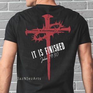 Op de afbeelding: Zwart t-shirt met een rood kruisontwerp, met een doornenkroon en de tekst "IT IS FINISHED John 19:30". Het ontwerp is gecentreerd op de achterkant van het shirt. De merknaam "JazNJezArts" staat onderaan.