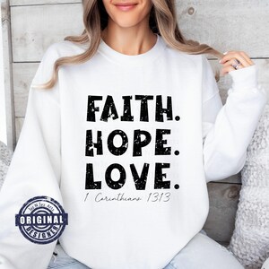 May include: White sweatshirt with black text that reads "FAITH. HOPE. LOVE. 1 Corinthians 13:13".