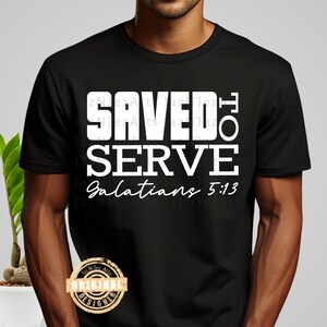 May include: Black t-shirt with the text "SAVED TO SERVE" in bold white letters, with "Galatians 5:13" in a script font. The shirt also features a gold and brown "ORIGINAL DESIGNER" logo.