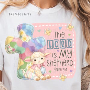 Pode incluir: Camiseta branca com uma cruz de retalhos colorida e um cordeiro com um laço rosa. O texto "The LORD is MY SHEPHERD" é exibido em um fundo rosa com flores e corações. Salmo 23:1 também está incluído.