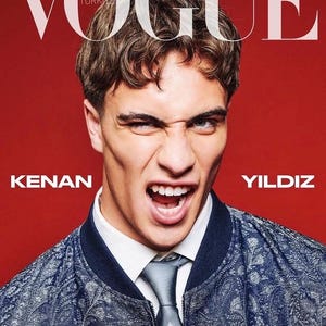 Può includere: Una copertina di rivista con il testo VOGUE TURKIYE e KENAN YILDIZ. Una persona con capelli castani corti indossa un bomber blu a motivi sopra una camicia bianca con colletto e una cravatta grigia, su uno sfondo rosso solido.