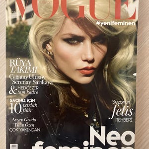 May include: Vogue Türkiye magazine cover featuring a woman with blonde hair and bold makeup. The cover includes the text "Neo feminen" and other Turkish text. The magazine has a glossy finish.