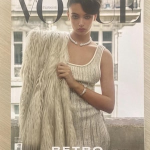 Könnte beinhalten: Vogue Türkiye-Magazin-Cover. Eine Frau in einem paillettenbesetzten Kleid und Schmuck hält einen Kunstfellmantel. Der Text auf dem Cover lautet "VOGUE" und "RETRO İHTİŞAM."