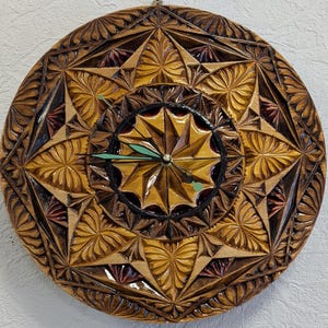 May include: A round, wooden clock with intricate carved geometric and floral patterns. The clock face features a starburst design with a black border and green clock hands. The clock is primarily brown and gold in color.