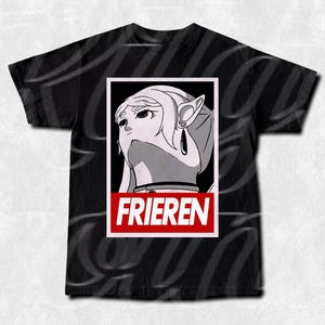 May include: Black t-shirt with a graphic of a female anime character with long white hair and pointed ears. The character is framed in a white rectangle with the word "FRIEREN" in red block letters at the bottom. The shirt has a crew neck.