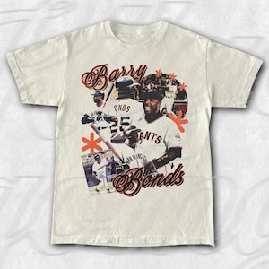 Peut inclure: T-shirt crème avec un collage du joueur de baseball Barry Bonds. Le design comprend des images de Bonds en action, le nom "Barry Bonds" dans une écriture stylisée et le nom de l'équipe "Giants". Des accents orange complètent le design.
