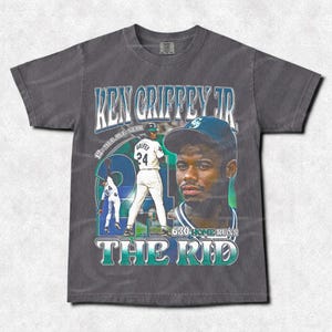 May include: Dark gray t-shirt featuring a graphic of baseball player Ken Griffey Jr. The design includes his name, a portrait, and the text "The Kid." The shirt has a vintage, distressed look.