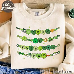May include: A white sweatshirt with a green, shamrock-themed design that reads "Happy St. Patrick's Day". The design features a string of shamrocks, hearts, and other St. Patrick's Day symbols.