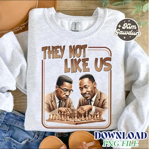 May include: A light gray sweatshirt with the text "THEY NOT LIKE US" in brown letters. The graphic features illustrations of two men playing chess. The sweatshirt has a crew neck and long sleeves.