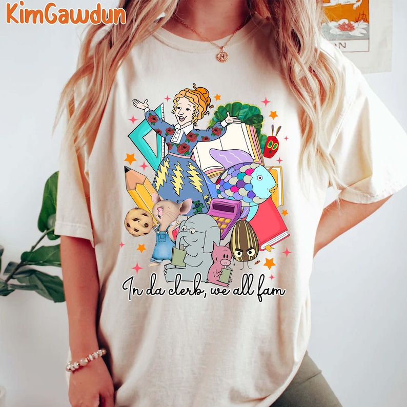 May include: A white t-shirt with a colorful graphic print of a teacher and students. The graphic includes a teacher with a microphone, a fish, a book, a pencil, a cookie, a mouse, an elephant, a pig, and a seed. The text "In da clerk, we all fam" is printed below the graphic.