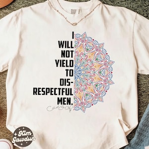 Puede incluir: Camiseta color crema con el texto "I WILL NOT YIELD TO DIS-RESPECTFUL MEN." y un diseño de mandala colorido. El diseño incorpora elementos azules, amarillos, rojos y verdes. La camiseta tiene cuello redondo y mangas cortas.