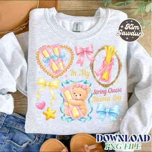 Puede incluir: Sudadera gris claro con un diseño gráfico colorido. El diseño incluye ilustraciones de queso en hebra, lazos, un osito de peluche y el texto "In My String Cheese Mama Era".