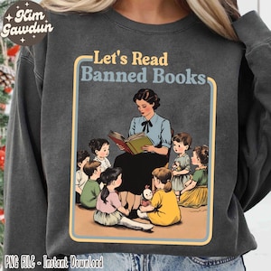 May include: A gray sweatshirt with a vintage-style illustration of a teacher reading a book to a group of children. The text "Let's Read Banned Books" is printed in yellow and black on the sweatshirt.