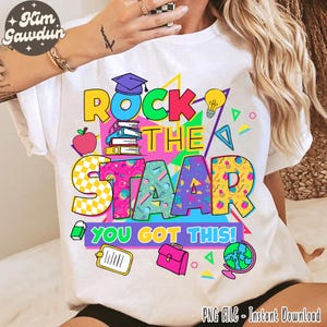 May include: White t-shirt with a colorful graphic that says "Rock the STAAR, You Got This!" The design includes a graduation cap, books, an apple, a lightbulb, and other school-themed elements. The shirt is a PNG file for instant download.