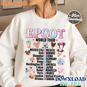 Puede incluir: Sudadera blanca con la inscripción "EPCOT WORLD TOUR" en una fuente colorida y con forma de burbuja. El diseño incluye varios gráficos de alimentos e iconos que representan diferentes ciudades y países.
