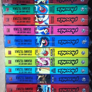 May include: A stack of 12 colorful graphic novels, all featuring the same character, a rooster with a red comb and a yellow beak. The books are titled "Phoonix" and are numbered from 1 to 12. Each book has a different color and a different title, such as "Dawn", "Future", "Karma", "Resurrection", "Nostalgia", "Civil War Part One", "Civil War Part Two", "Strange Beasts Life", "Sun Part One", "Sun Part Two", and "Early Works".