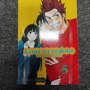 May include: Volume 5 of the manga series "kimi ni todoke: From Me to You" by Karuho Shiina. The cover features three characters, two girls and a boy, with the boy smiling and the girls looking surprised. The background is yellow with a red and green title.