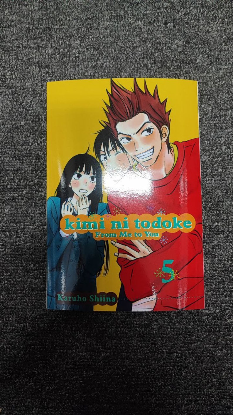 May include: Volume 5 of the manga series "kimi ni todoke: From Me to You" by Karuho Shiina. The cover features three characters, two girls and a boy, with the boy smiling and the girls looking surprised. The background is yellow with a red and green title.
