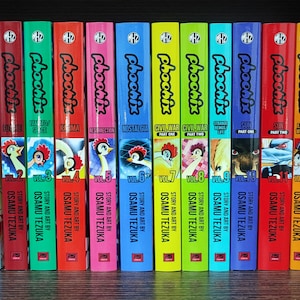 May include: A collection of 12 colorful graphic novels titled "Phoonix" by Osamu Tezuka. The books are arranged in order from volume 1 to volume 12. Each volume has a different cover design and title, including "Dawn", "Forever", "20th Century", "Karma", "Resurrection", "Nostalgia", "Civil War Part One", "Civil War Part Two", "Change to Survive", "Sun Part One", "Sun Part Two", and "Early Works".