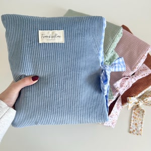 May include: A selection of corduroy baby changing mats in shades of blue, green, pink, and brown. Each mat has a patterned fabric trim and a coordinating bow. The blue mat displays a label reading "Frankie Rae Handmade."