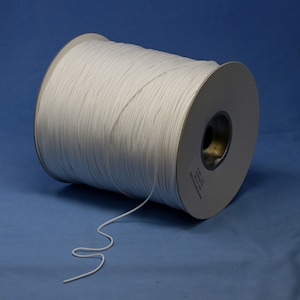 May include: A spool of white cord, wound around a cardboard tube. The cord is about 6mm thick and is unwinding from the spool.