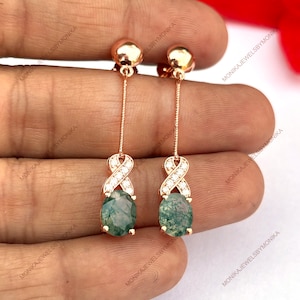 May include: A pair of dangle earrings with a green agate stone and a silver infinity symbol with clear cubic zirconia stones. The earrings are on a rose gold chain.