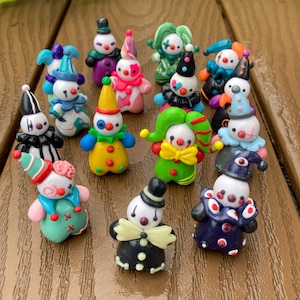 Pode incluir: Uma coleção de figuras de palhaços coloridos e feitos à mão. Cada figura apresenta um design único com cores vibrantes, incluindo vermelho, azul, verde, amarelo e rosa. Os palhaços têm vários chapéus, golas e roupas.