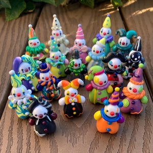 May include: A collection of small, handcrafted clown figurines made from colourful polymer clay. Each miniature figure features a distinct outfit, including patterned hats, ruffled collars, and vibrant colour combinations like orange, purple, green, and black.