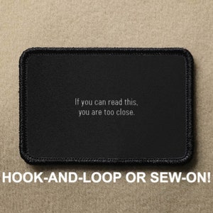 May include: Black rectangular patch with white text that reads "If you can read this, you are too close." The patch has a black border and is labelled "HOOK-AND-LOOP OR SEW-ON!"