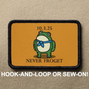 Puede incluir: Parche rectangular con una rana de dibujos animados con una corbata azul, sobre un fondo naranja. El texto "10.3.25" está encima de la rana y "NEVER FROGET" debajo. El parche tiene un borde negro.