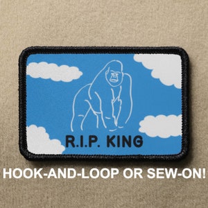 Puede incluir: Un parche bordado azul y blanco con un contorno negro. El parche presenta un gorila de dibujos animados con el texto "R.I.P. KING" debajo. El parche está diseñado para ser fijado con velcro o cosido.