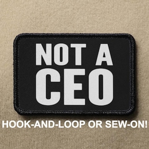 May include: Black patch with white text that reads "NOT A CEO". The patch has a black border and is designed to be attached with hook-and-loop or sewn on.